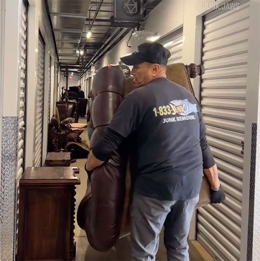 A Junk Jaws crew member carrying a leather chair out of a storage unit hallway